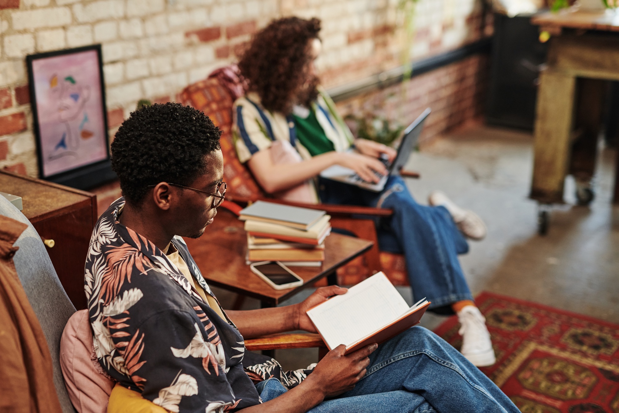 African American guy reading book while sitting in armchair in living room African American guy reading book while sitting in armchair in living room